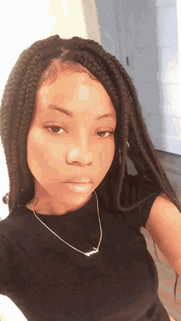 a young woman with braids is wearing a black shirt and a gold necklace
