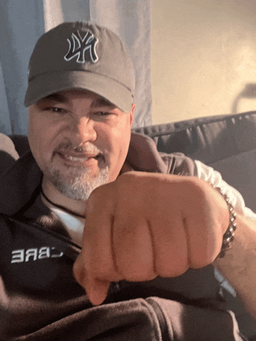 a man wearing a ny hat holds his fist up in front of his face