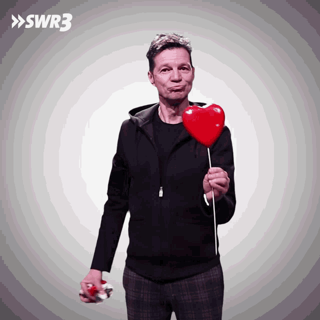a man holding a red heart shaped lollipop with swr3 on the bottom right