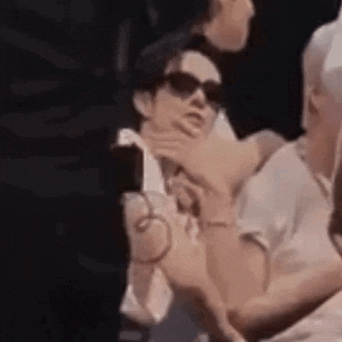 a man wearing sunglasses is holding another man 's hand while sitting next to another man .