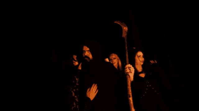 a man with a beard is holding a sword while two women look on