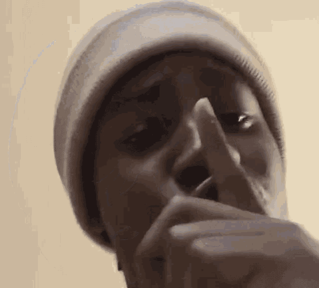 a man wearing a beanie is holding his finger to his lips .