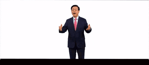a man in a suit and pink tie is speaking in front of a wall that says more