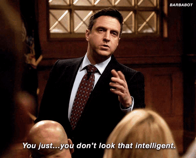 a man in a suit and tie talks to a group of people and says " you just ... you don 't look that intelligent "