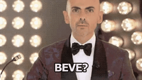 a man in a tuxedo and bow tie is standing in front of a microphone and saying beve .
