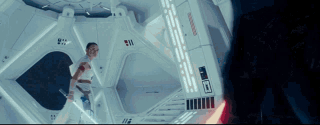 a woman is holding a lightsaber in a room with a red light behind her
