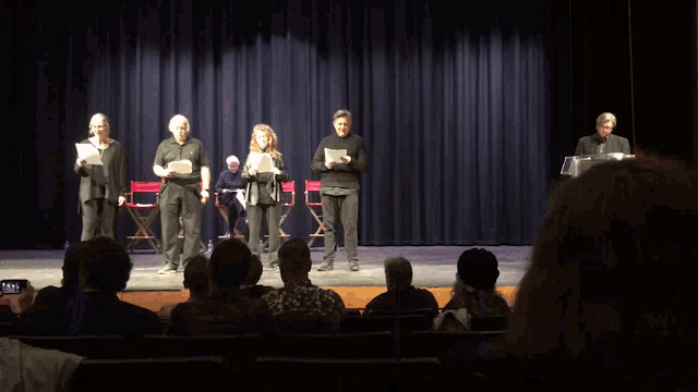 a group of people standing on a stage holding papers in front of a blue curtain