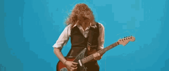 a man with curly hair is playing an electric guitar in front of a blue background