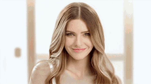 a woman with long blonde hair is smiling for the camera while wearing a white tank top .