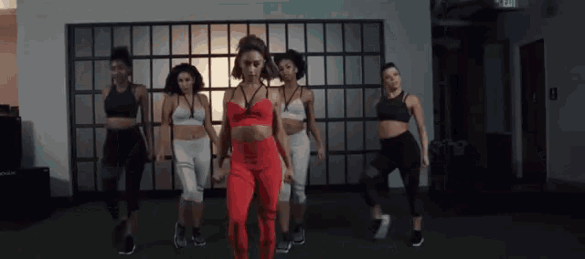 a group of women are dancing in a room with a green exit sign