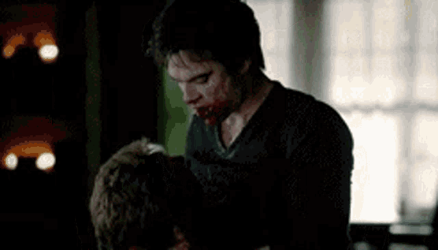a man with blood on his face is holding another man in a dark room .