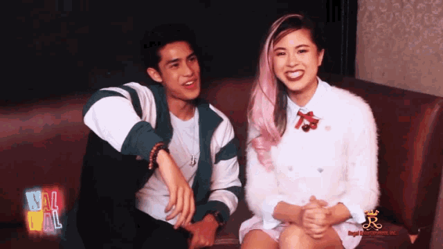 a man and a woman are sitting on a couch with a neon sign that says wall wall