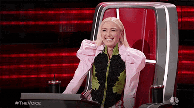 a woman in a pink jacket is sitting in a chair on nbc 's the voice