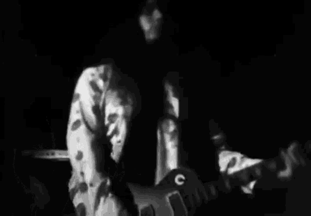 a black and white photo of a man playing a guitar .