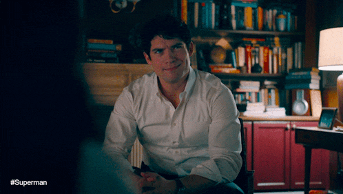 a man in a white shirt is sitting in front of a bookshelf with the hashtag #superman on the bottom