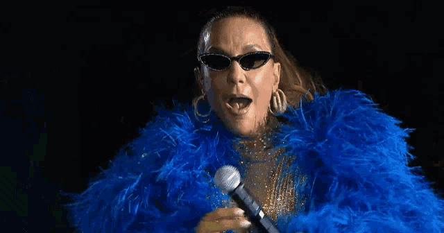 a woman is singing into a microphone while wearing a blue feathered coat