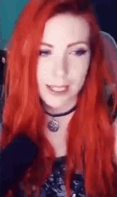 a woman with red hair is smiling and wearing a choker necklace