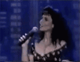 a woman is singing into a microphone while a man looks on .
