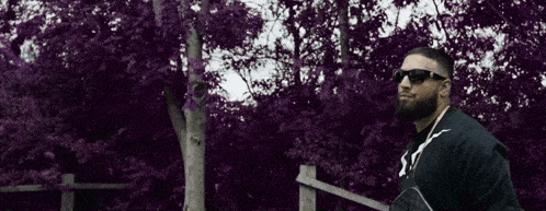 a man wearing sunglasses is standing in front of a purple tree