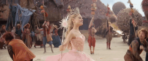 a woman in a pink dress is holding a wand and a crown .