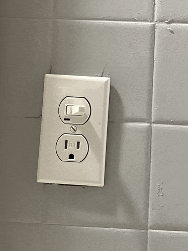 a white electrical outlet on a tiled wall has a light switch on it
