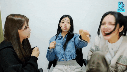 three women are sitting in a room and one has a tattoo on her face