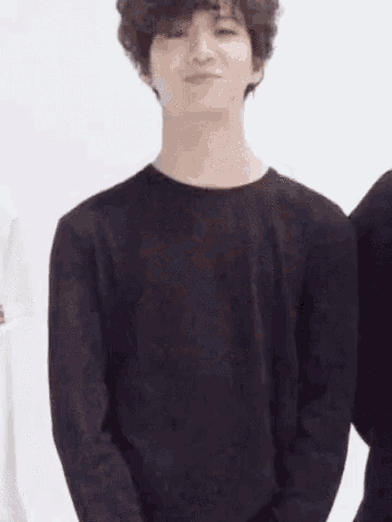 a young man with curly hair is wearing a black sweater and standing in front of a white wall .