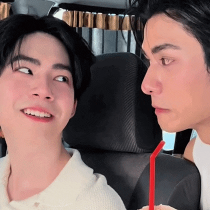 two men are sitting next to each other in a car and one of them is drinking from a red straw .