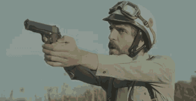 a man wearing a helmet and goggles is pointing a gun in a field .