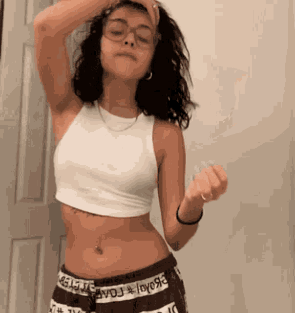 a woman wearing glasses and a white crop top is standing in front of a door