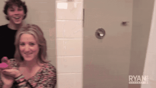 a man and a woman are standing in a bathroom with the word ryan on the bottom left