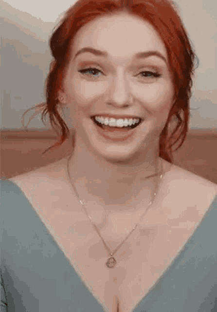 a woman with red hair is smiling and wearing a blue dress and a necklace .