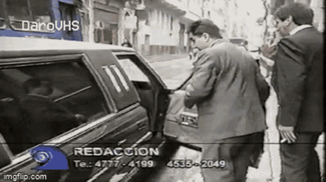 a man in a suit is getting out of a car while two other men look on .