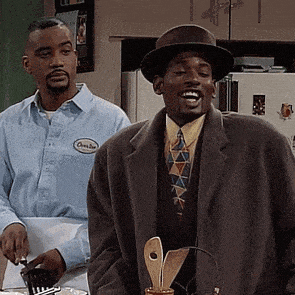 a man wearing a hat is standing next to another man in a kitchen .