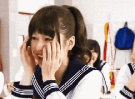 a girl in a school uniform is covering her face with her hands while laughing .