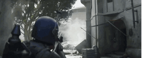 a man in a blue helmet is standing in front of a building holding a gun in his hand .