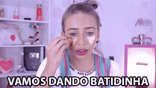 a woman is applying makeup and the words vamos dando batidinha are written above her