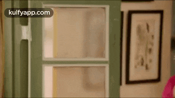 a woman is standing in front of a green door in a room with a picture on the wall .