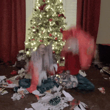 a girl sitting in front of a christmas tree covered in gifts