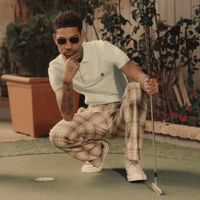 a man wearing sunglasses is kneeling down holding a golf club on a green