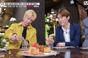 two men are sitting at a table with plates of food and a sign that says m.