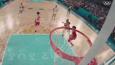 a basketball game is being played in front of a crowd with the olympic rings visible