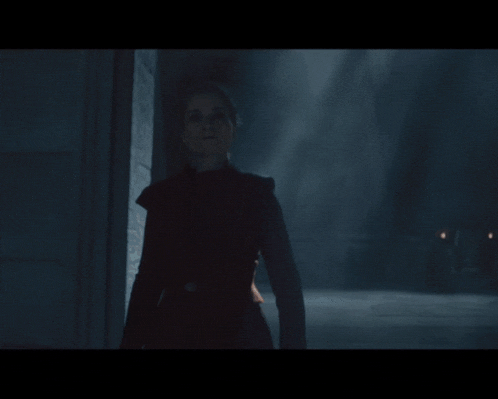 a woman in a black coat is standing in a dark hallway