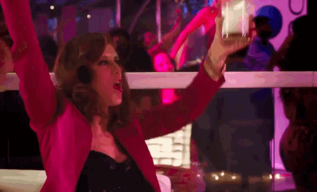 a woman in a pink jacket is holding a glass in her hand in a club .