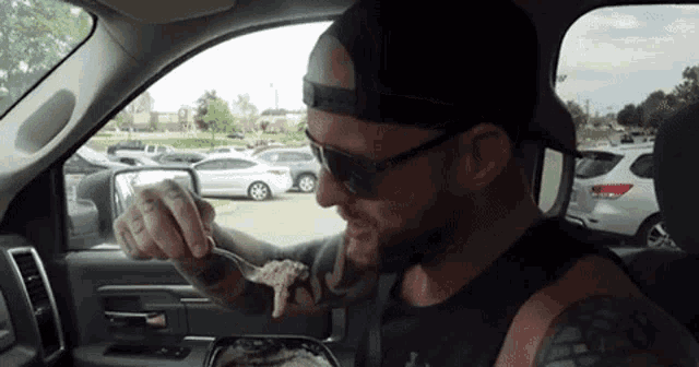 a man is sitting in a car eating food with a fork