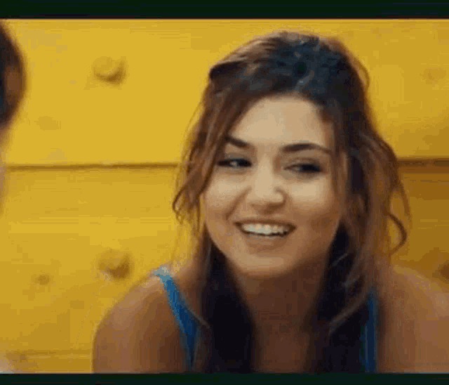 a woman in a blue tank top is smiling in front of a yellow background .