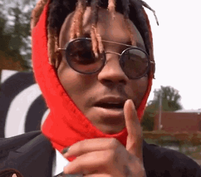 a man wearing sunglasses and a red scarf around his head is making a funny face .