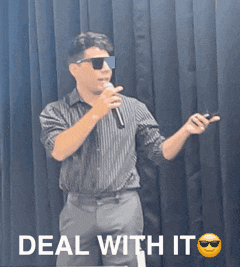 a man wearing sunglasses holds a microphone in front of a black curtain with the words deal with it below him