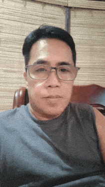 a man wearing glasses sits in a chair and looks at the camera