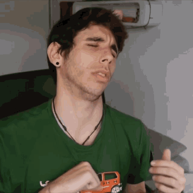 a man wearing a green shirt with a toy car on it is making a funny face